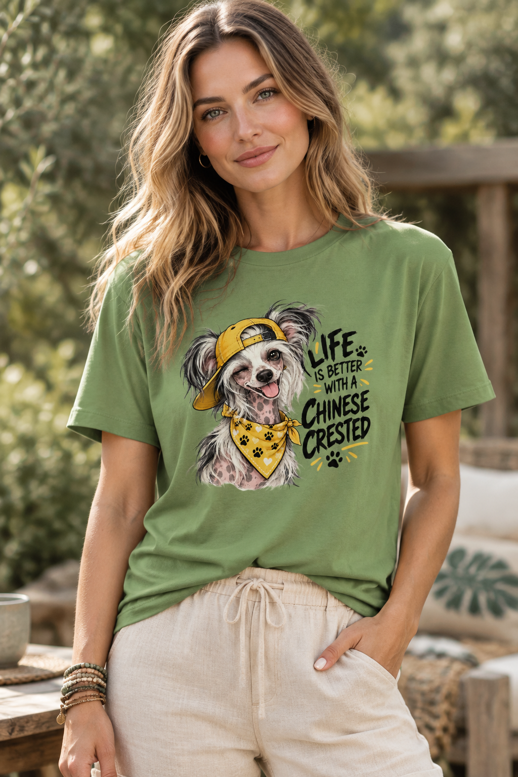 Woman in green t-shirt with dog print, beige pants, standing outdoors, trees in background.